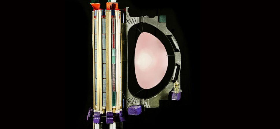 A “toy”-sized, but accurately scaled, version of the ITER central solenoid (left) with one of the 18 toroidal field coils, printed on a desktop 3D printer. The pink oval represents the plasma. Notice the action figure at right showing the model’s scale. Photo: US ITER/ORNL