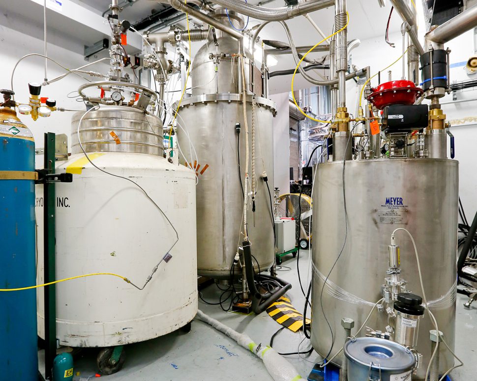 A view of the test environment at the Spallation Neutron Source shows a white tank containing helium on the left, the prototype cryoviscous compressor pump in the middle, and the valve box, which monitors the flow rate to the pump, on the right.